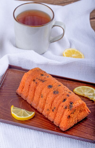 Vue latérale du gâteau aux raisins secs avec des tranches de citron sur une planche de bois et une tasse de thé sur une nappe