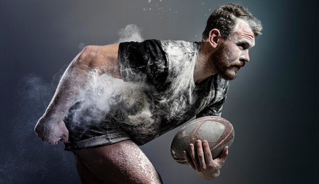 Vue latérale du joueur de rugby masculin athlétique tenant le ballon avec de la poussière