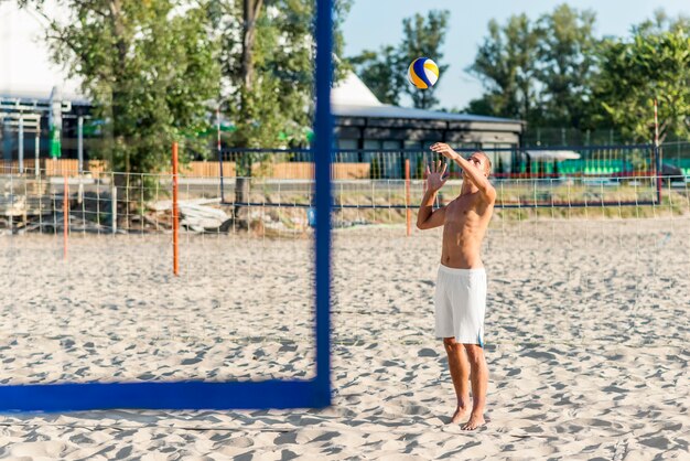 Vue latérale du joueur de volley-ball masculin torse nu pratiquant avec ballon sur la plage