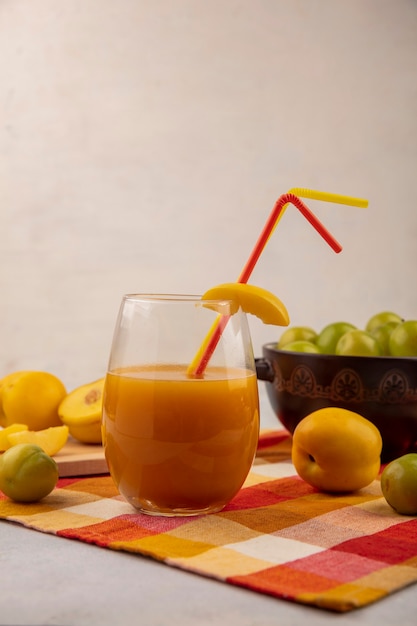 Vue Latérale Du Jus De Pêche Jaune Doux Frais Sur Un Verre Avec Des Pêches Fraîches Avec Des Prunes Cerises Vertes Sur Un Arc Sur Un Fond Blanc