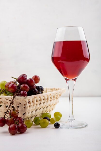 Vue latérale du jus de raisin noir en verre à vin et panier de raisins avec des baies de raisin sur fond blanc