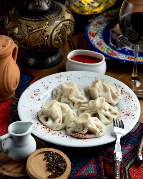 Vue latérale du khinkali géorgien traditionnel avec sumakh et sauce épicée sur une plaque blanche