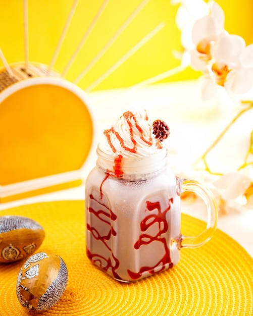 Vue latérale du lait frappé aux framboises avec de la crème fouettée dans un bocal en verre sur jaune