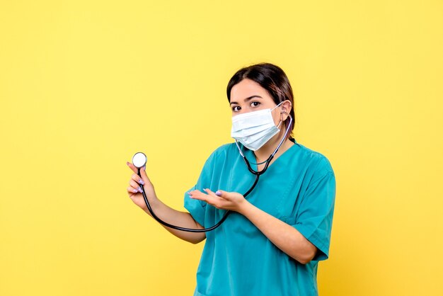 Vue latérale du médecin en uniforme médical en masque pointe vers le phonendoscope