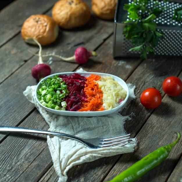 Vue latérale du mélange de légumes bouillis pommes de terre carottes betteraves servies avec des oignons verts hachés frais dans un bol blanc