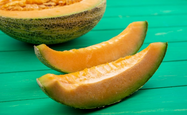 Vue latérale du melon cantaloup délicieux et tranché sur une surface en bois vert