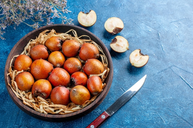 Vue latérale du mespilus germanica entier et haché à l'intérieur et à l'extérieur d'un bol marron à côté d'une fourchette sur une surface bleue