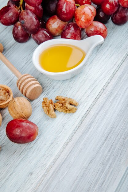 Vue latérale du miel avec une cuillère à miel en bois, des raisins frais et des noix sur une table en bois gris