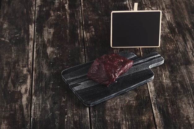 Vue latérale du morceau brut de luxe de steak de viande de baleine sur le bureau de coupe en pierre de marbre noir et table en bois vintage et étiquette de prix de tableau de craie