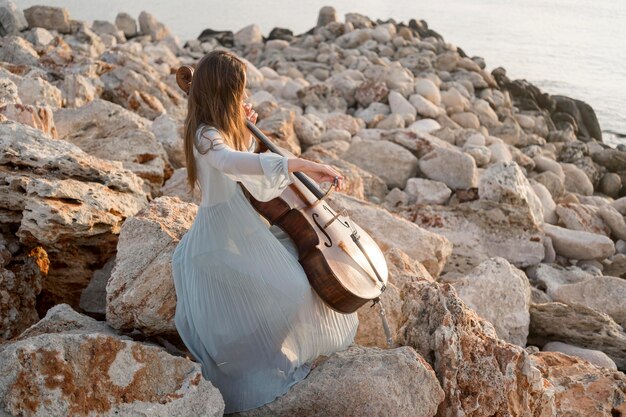 Vue latérale du musicien jouant du violoncelle sur les rochers