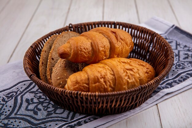 Vue latérale du pain comme croissant et tranches de pain d'épi brun épépiné dans le panier sur tissu sur fond de bois