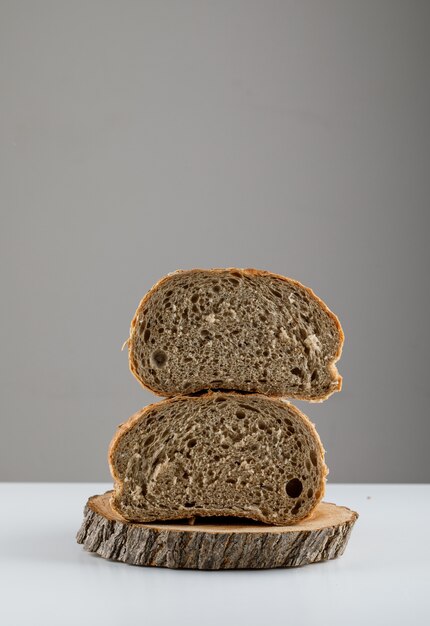 Vue latérale du pain en tranches sur du bois sur une surface blanche. espace vertical pour le texte