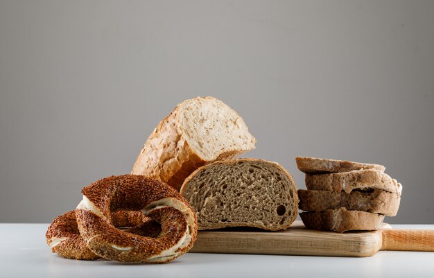 Vue latérale du pain en tranches sur une planche à découper avec bagel turc sur tableau blanc et surface grise. espace horizontal pour le texte