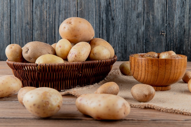 Photo gratuite vue latérale du panier et bol plein de pommes de terre sur un sac sur la surface en bois et l'arrière-plan avec copie espace