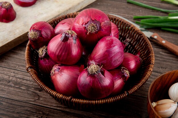 Vue latérale du panier plein d'oignons rouges sur fond de bois