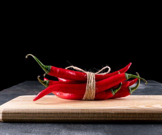 Vue latérale du piment rouge sur une planche à découper en bois sur fond noir