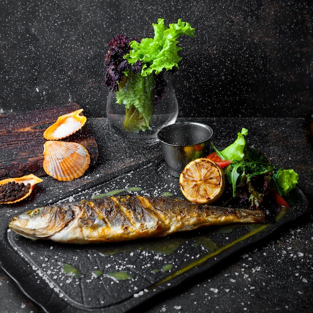 Vue latérale du poisson frit avec roquette et citron et tomate et sauce dans le bac