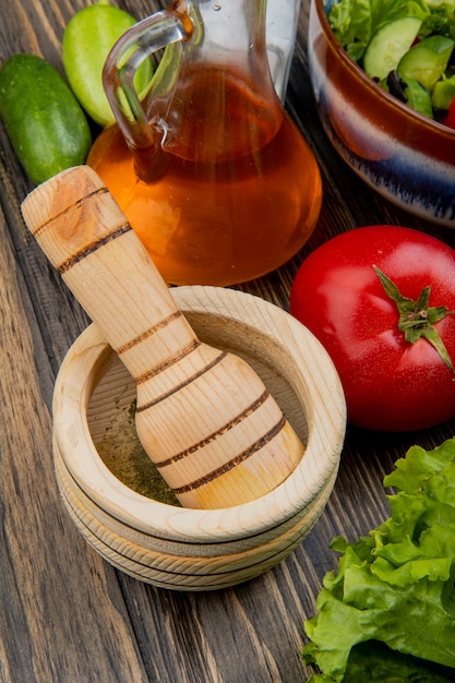 Vue latérale du poivre noir dans un broyeur d'ail avec de l'huile de laitue fondue tomate concombre sel et salade de légumes sur la surface en bois