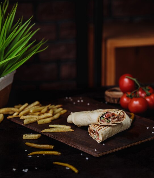 Vue latérale du poulet doner enveloppé dans du lavash et des frites sur une planche à découper en bois