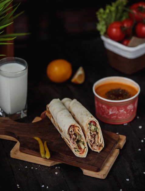 Vue latérale du poulet doner enveloppé dans du lavash sur une planche de bois servi avec une soupe au linteau et une boisson ayran sur la table