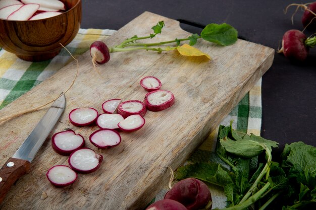 Vue latérale du radis rouge en tranches avec un couteau sur une surface en bois sur fond de tissu et marron