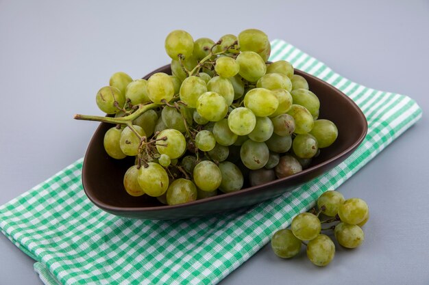 Vue latérale du raisin blanc dans un bol sur tissu à carreaux sur fond gris