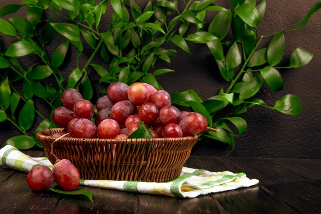 Vue latérale du raisin doux frais dans un panier en osier sur une surface en bois sur une table de feuilles vertes