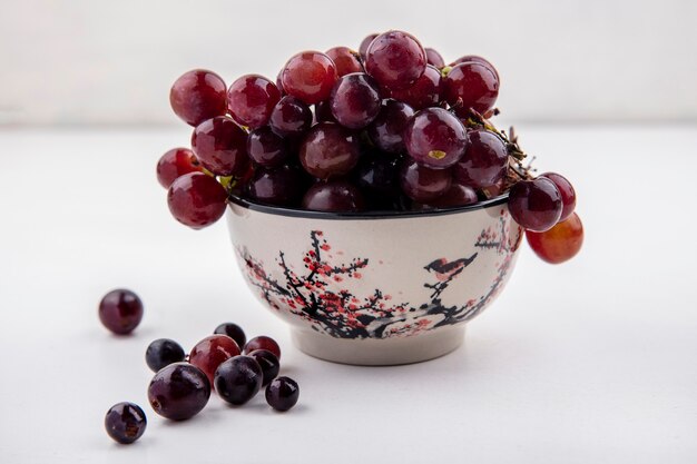 Vue latérale du raisin rouge dans un bol et sur fond blanc