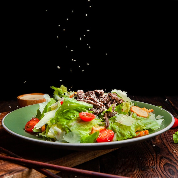 Vue latérale du riz coulant sur un délicieux repas de salade en plaque avec des baguettes sur fond en bois et noir. espace pour le texte
