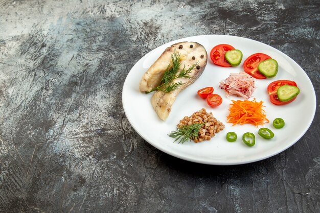 Vue latérale du sarrasin poisson bouilli servi avec des légumes verts sur une plaque blanche sur la surface de la glace