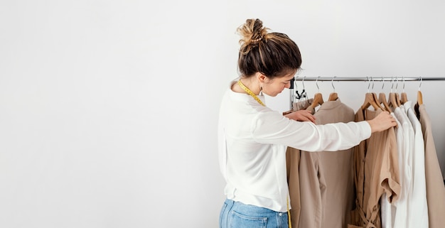 Vue latérale du tailleur féminin regardant à travers les vêtements sur cintres avec copie espace