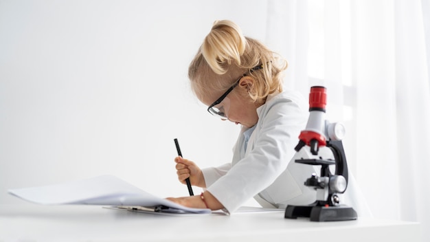 Vue latérale du tout-petit mignon avec blouse de laboratoire et microscope