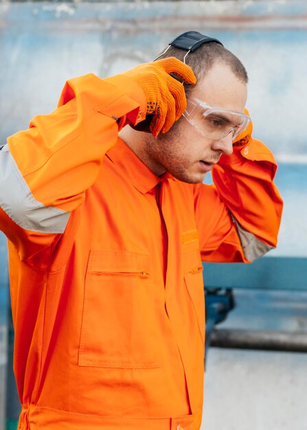 Vue latérale du travailleur masculin en uniforme avec des lunettes de protection et des écouteurs