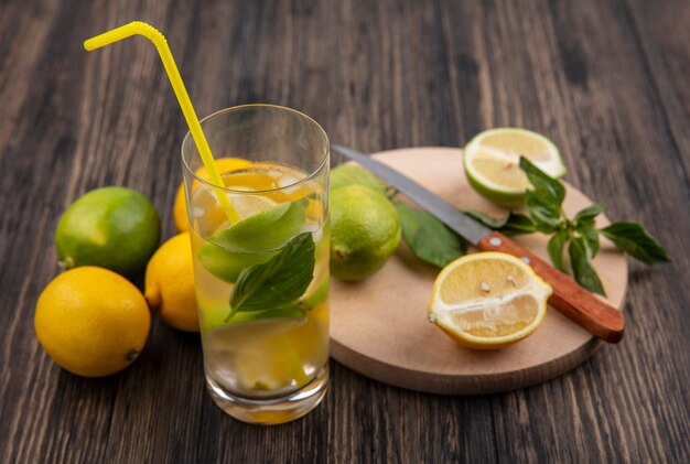 Vue latérale du verre d'eau avec des tranches de citron vert et de menthe avec de la paille jaune sur fond de bois