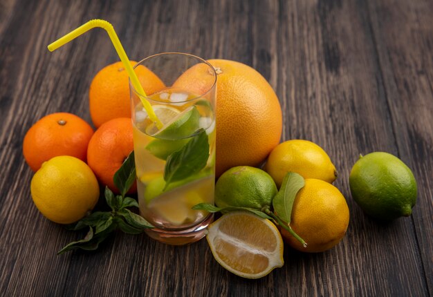 Vue latérale du verre d'eau avec des tranches de citron vert et de menthe avec paille jaune et pamplemousse aux oranges sur fond de bois