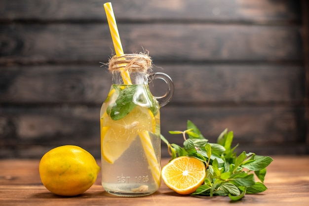 Vue latérale de l'eau de désintoxication fraîche naturelle servie avec de la menthe en tube et de l'orange sur fond marron