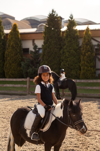 Photo gratuite vue latérale des enfants apprenant à monter à cheval