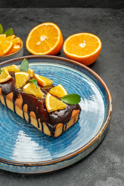 Photo gratuite vue latérale de l'ensemble de gâteaux savoureux d'oranges entières et coupées jaune avec fourchette et couteau sur table sombre