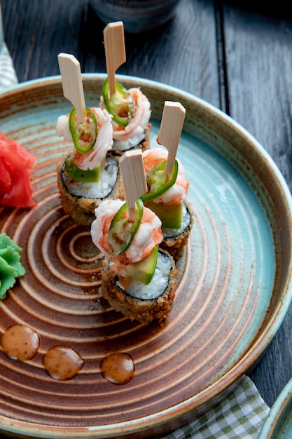 Vue latérale de l'ensemble de rouleaux de sushi cuit au four avec des crevettes servi avec du wasabi et du gingembre sur une plaque sur bois