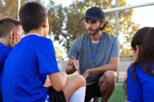 Vue latérale d'un entraîneur de football aidant les enfants