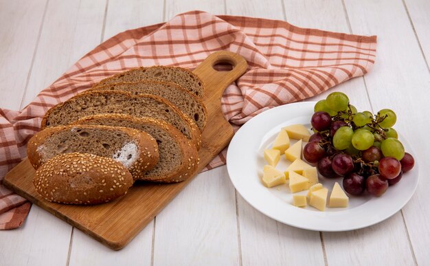 Vue latérale de l'épi semé brun tranché sur une planche à découper sur un tissu à carreaux et une assiette de fromage et de raisin sur fond de bois