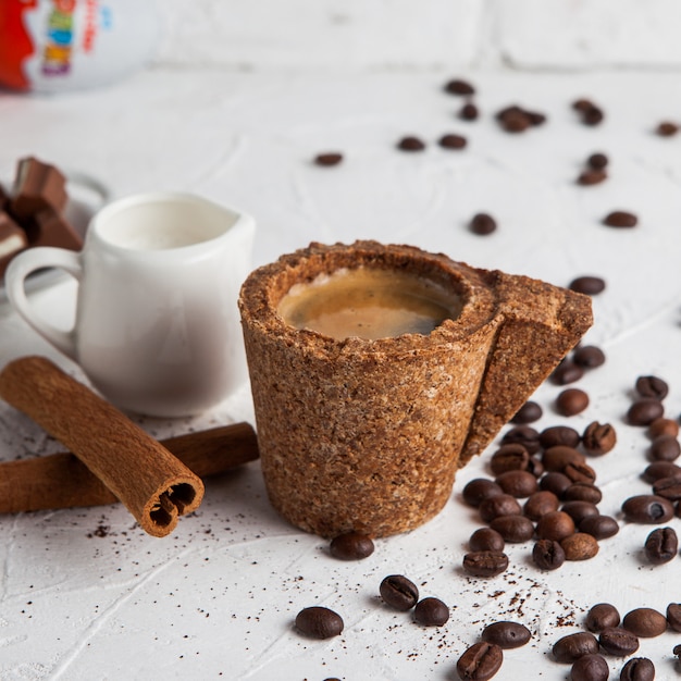Vue latérale expresso dans une tasse en liège avec carafe avec du lait, de la cannelle, des grains de café