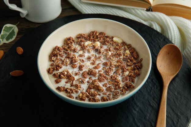 Vue latérale de la farine d'avoine avec du lait de noix et des amandes avec une cuillère en bois sur un dessous de plat sur fond de bois