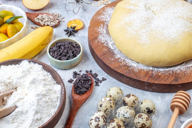 Vue latérale de la farine de pâtisserie crue sur une râpe à planche ronde oeufs de fruits frais sur fond blanc taché