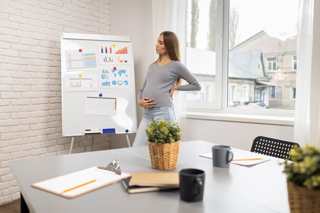 Vue latérale d'une femme d'affaires enceinte avec tableau blanc au bureau