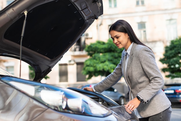 Vue latérale de la femme d'affaires vérifiant le moteur de la voiture