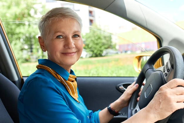 Vue latérale d'une femme d'âge moyen gaie à l'intérieur de la voiture sur le siège du conducteur avec les mains sur le volant