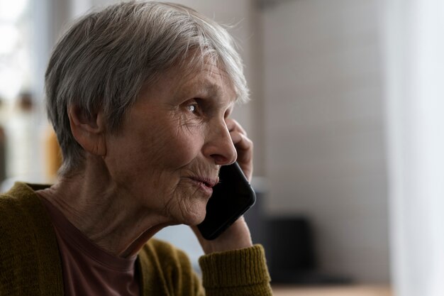 Vue latérale femme âgée parlant au téléphone à la maison