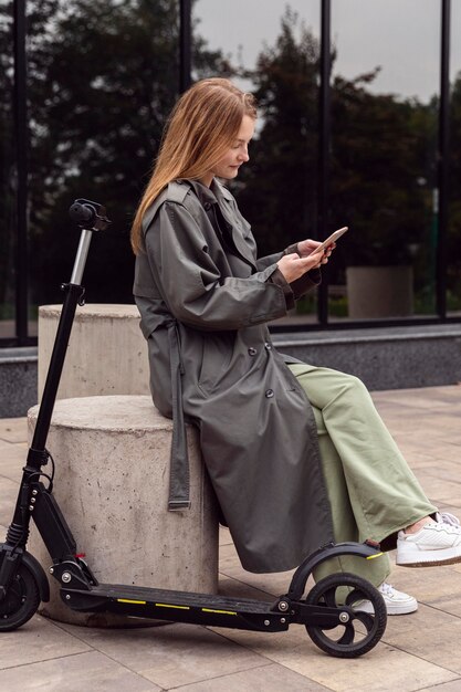 Vue latérale de la femme à l'aide de son smartphone à côté de scooter électrique