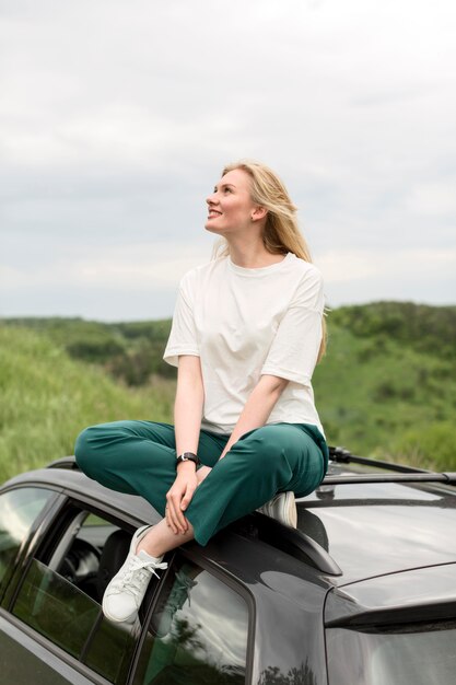 Vue latérale d'une femme appréciant la nature en se tenant debout sur la voiture